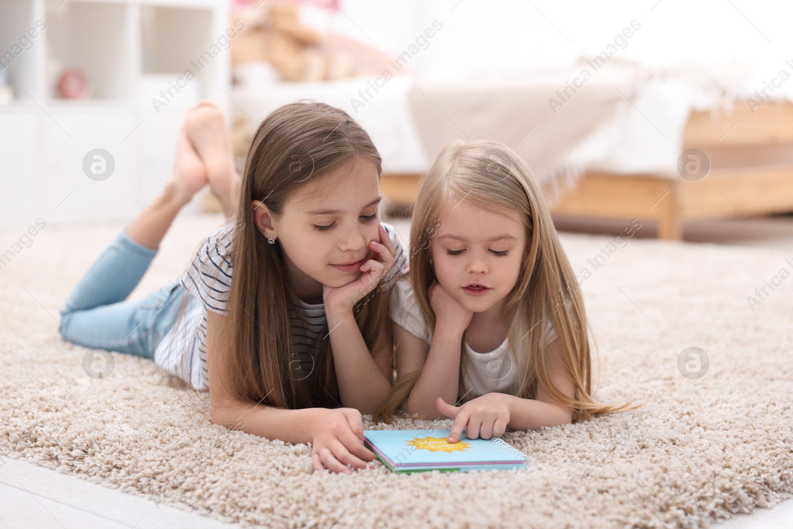 Photo of Cute little sisters reading book together at home