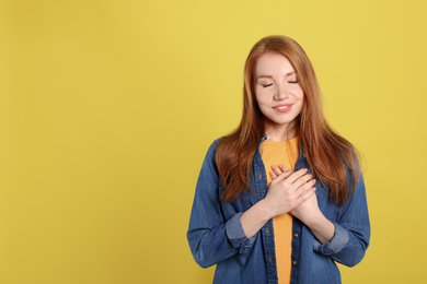 Photo of Beautiful grateful woman with hands on chest against yellow background. Space for text