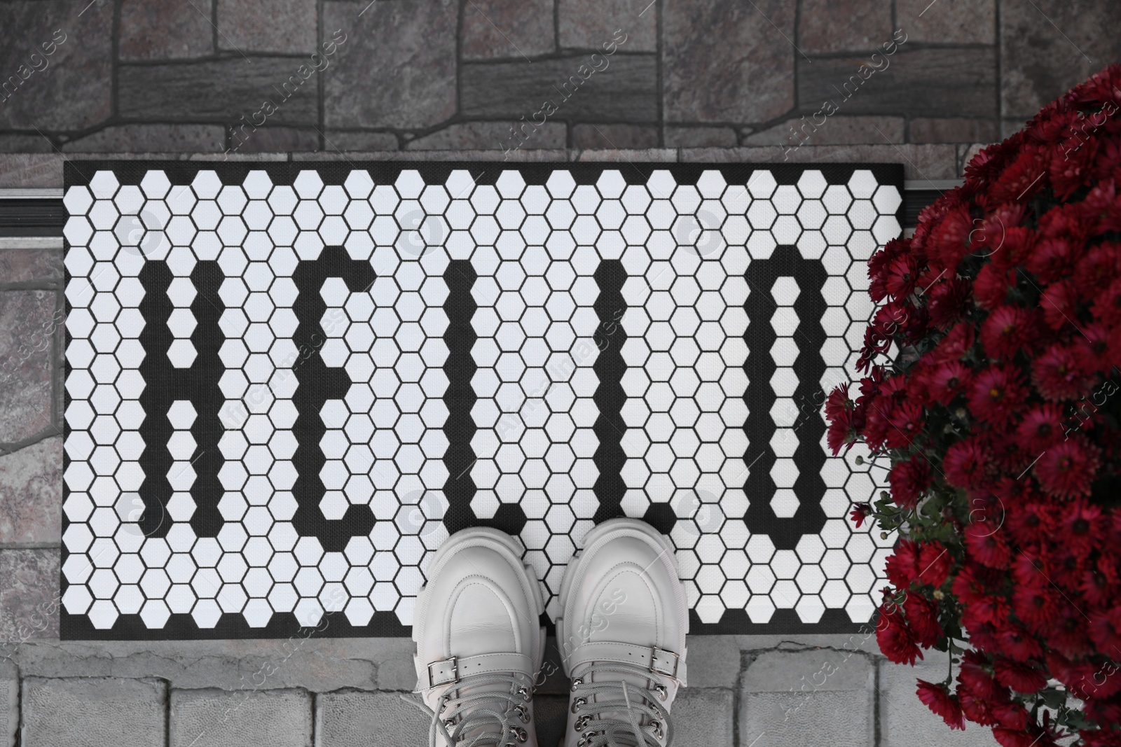 Photo of Stylish door mat with word Hello, shoes and beautiful flowers on stairs, flat lay