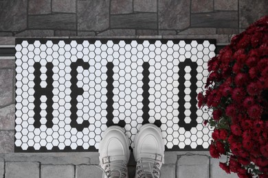 Photo of Stylish door mat with word Hello, shoes and beautiful flowers on stairs, flat lay