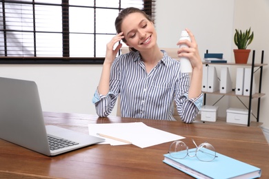 Photo of Young woman applying thermal water on face in office. Cosmetic product