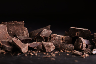 Photo of Pieces of dark chocolate on black table, closeup