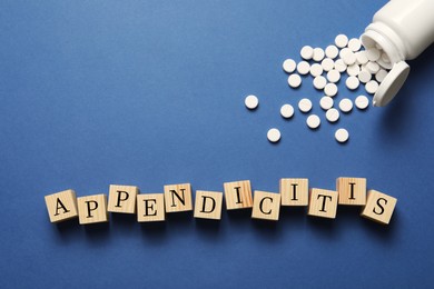 Photo of Word Appendicitis made of wooden cubes and jar with pills on blue background, flat lay. Space for text