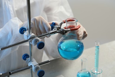 Photo of Scientist working with flask of light blue liquid in laboratory, closeup