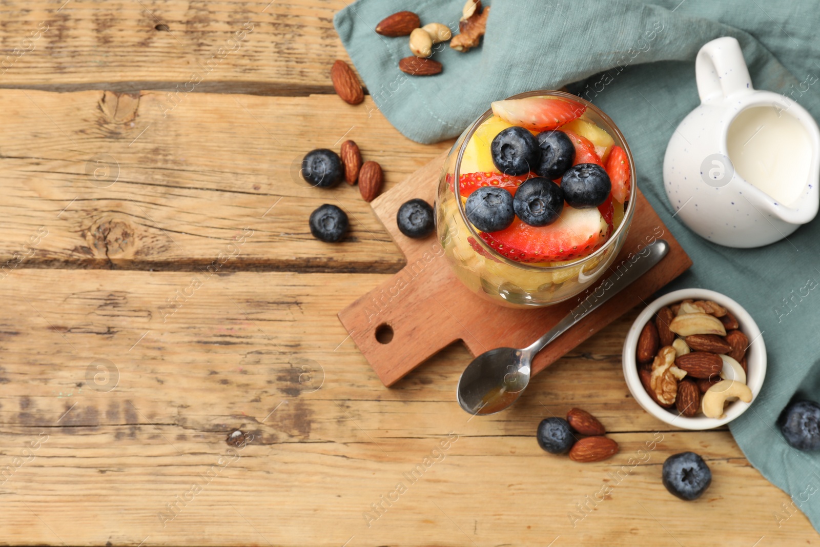 Photo of Delicious fruit salad, berries and nuts on wooden table, flat lay. Space for text