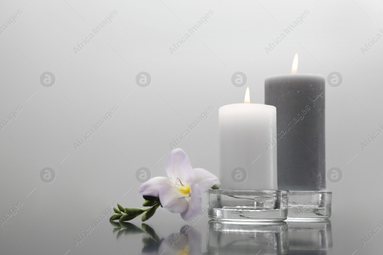 Photo of Wax candles in glass holders and flower on table against light background. Space for text