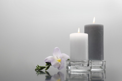 Wax candles in glass holders and flower on table against light background. Space for text