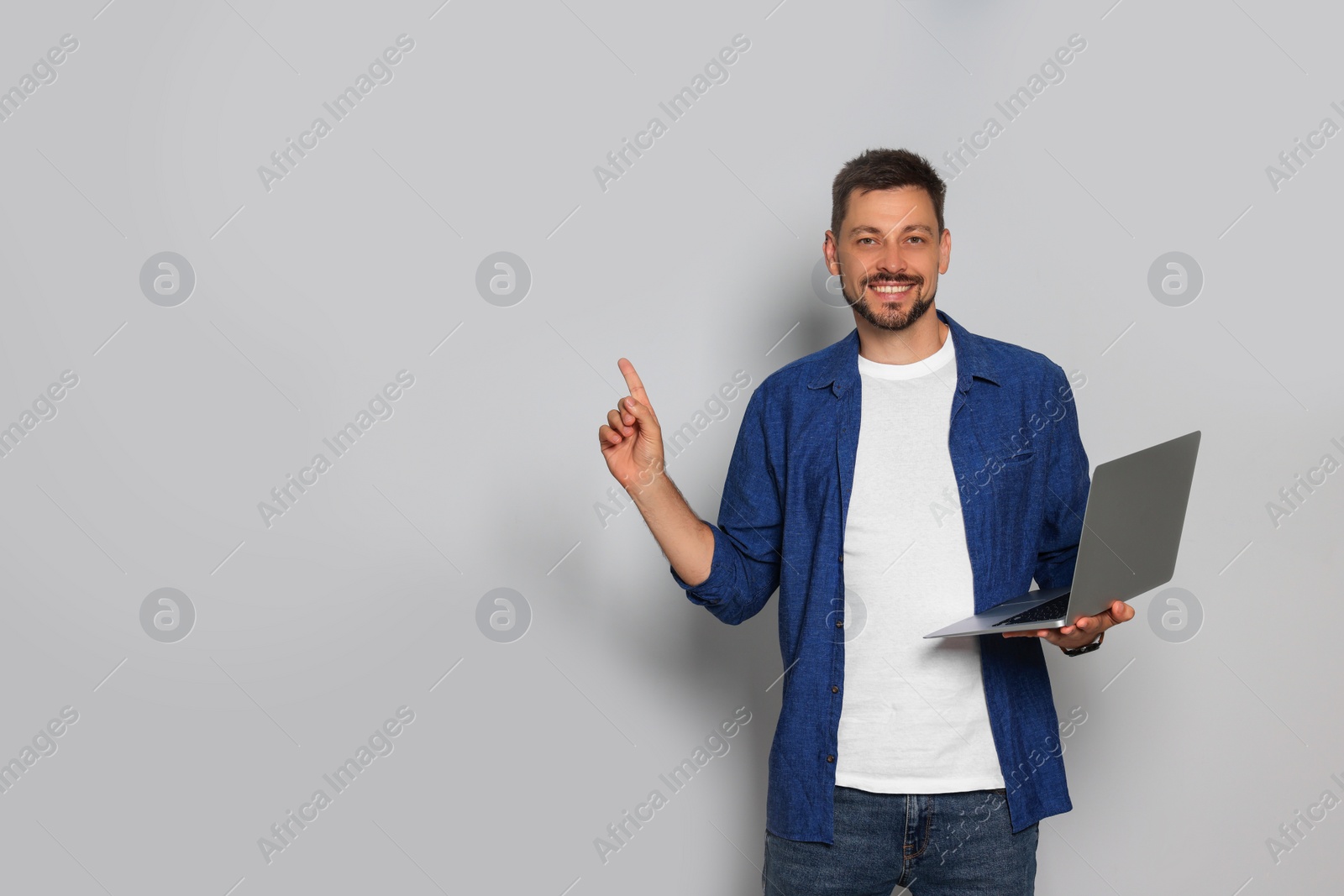 Photo of Smiling man with laptop on light grey background. Space for text