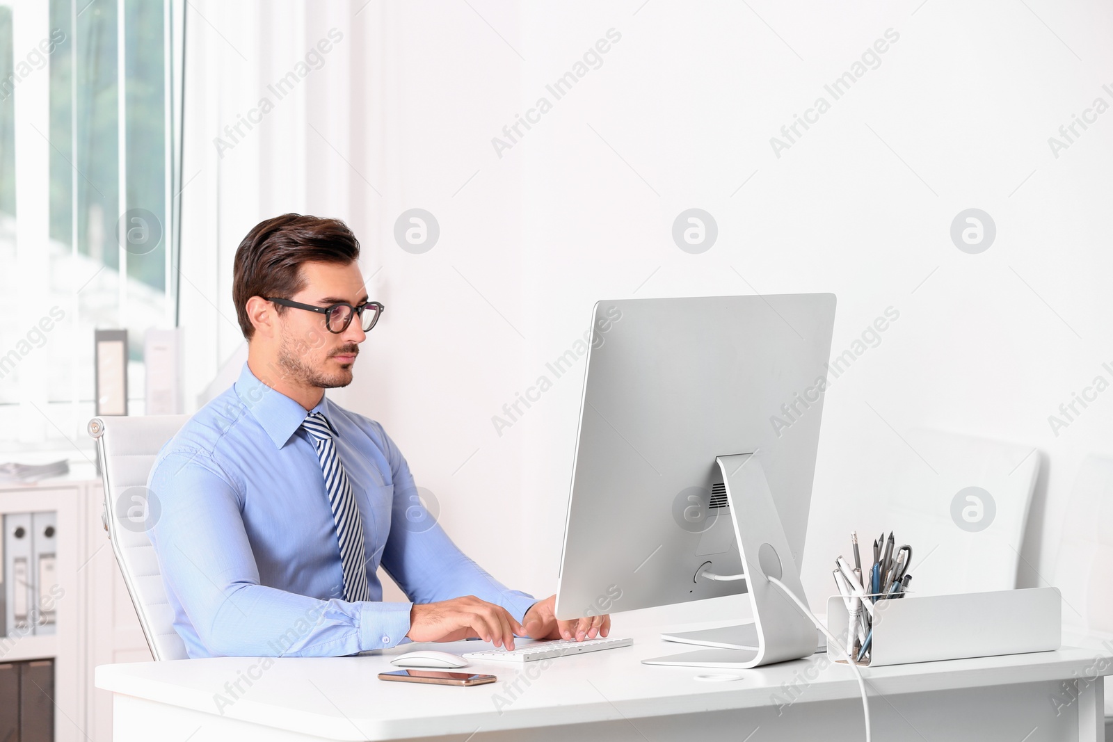 Photo of Handsome young man working with computer at table in office