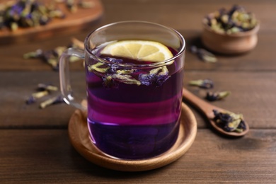 Photo of Glass mug of organic blue Anchan with lemon on wooden table. Herbal tea