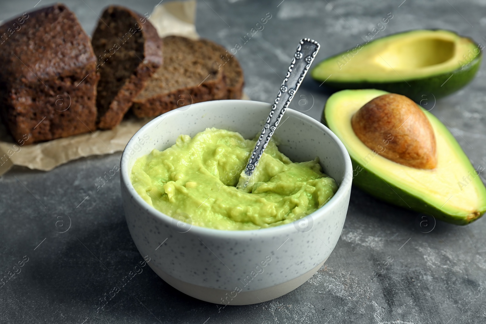 Photo of Bowl with guacamole, ripe avocado and bread on table
