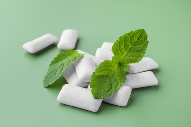 Photo of Tasty white chewing gums and mint leaves on light green background, closeup