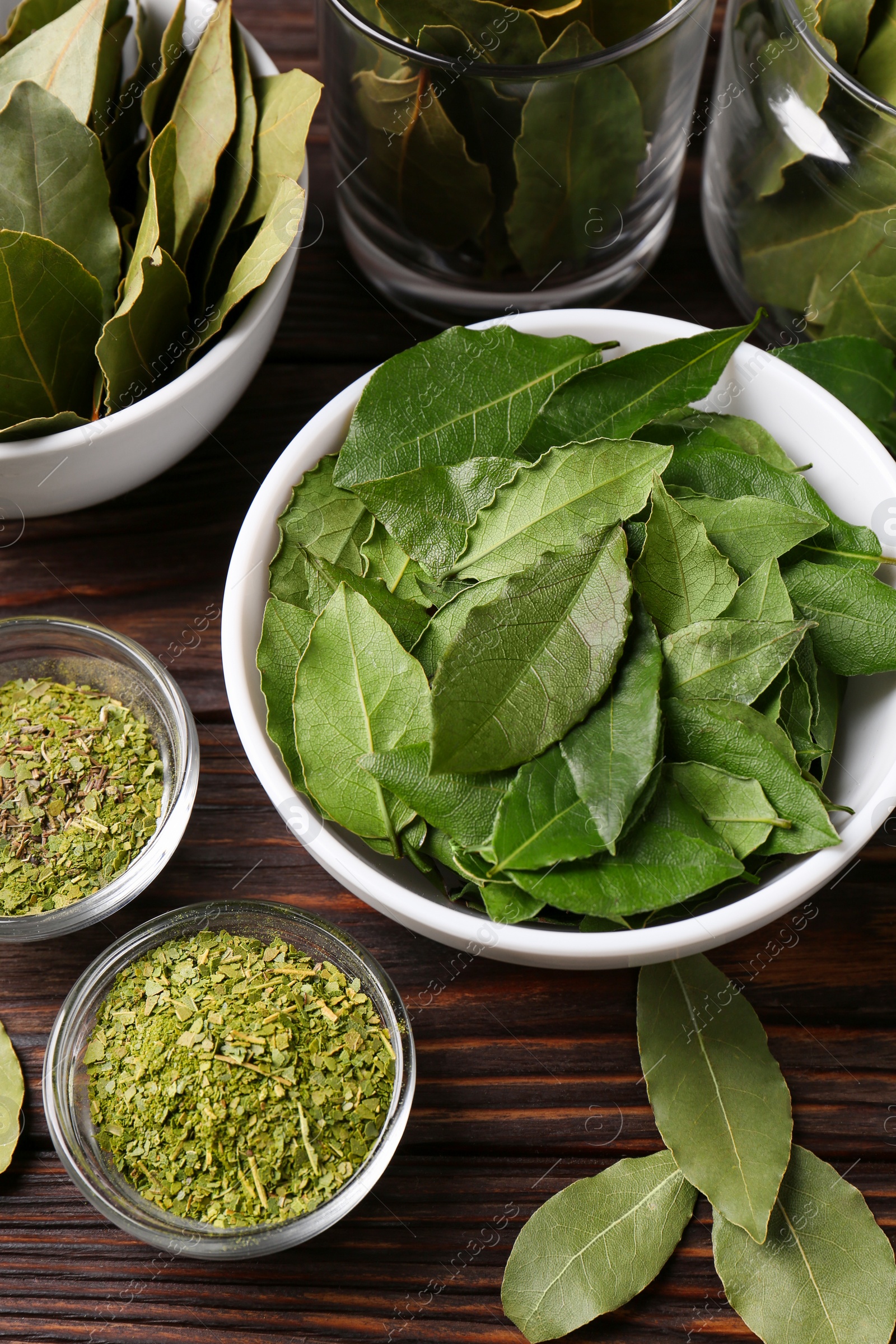 Photo of Bowls with ground, fresh and dry bay leaves on wooden table, view from above