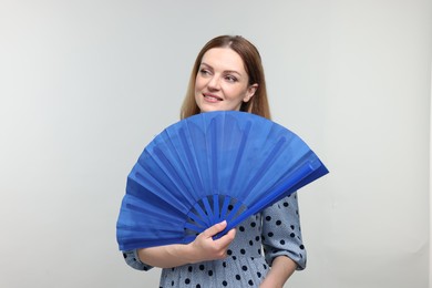 Happy woman with blue hand fan on light grey background