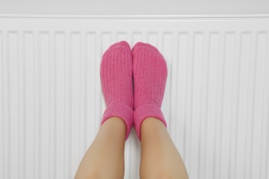 Photo of Woman warming legs on heating radiator near white wall, closeup