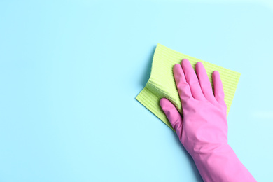 Photo of Person in rubber glove with rag on light blue background, closeup of hand. Space for text