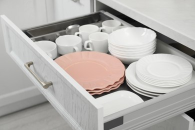 Photo of Clean plates, bowls and cups in drawer indoors