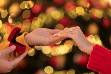 Photo of Making proposal. Woman with engagement ring and her fiance holding hands against blurred lights, closeup
