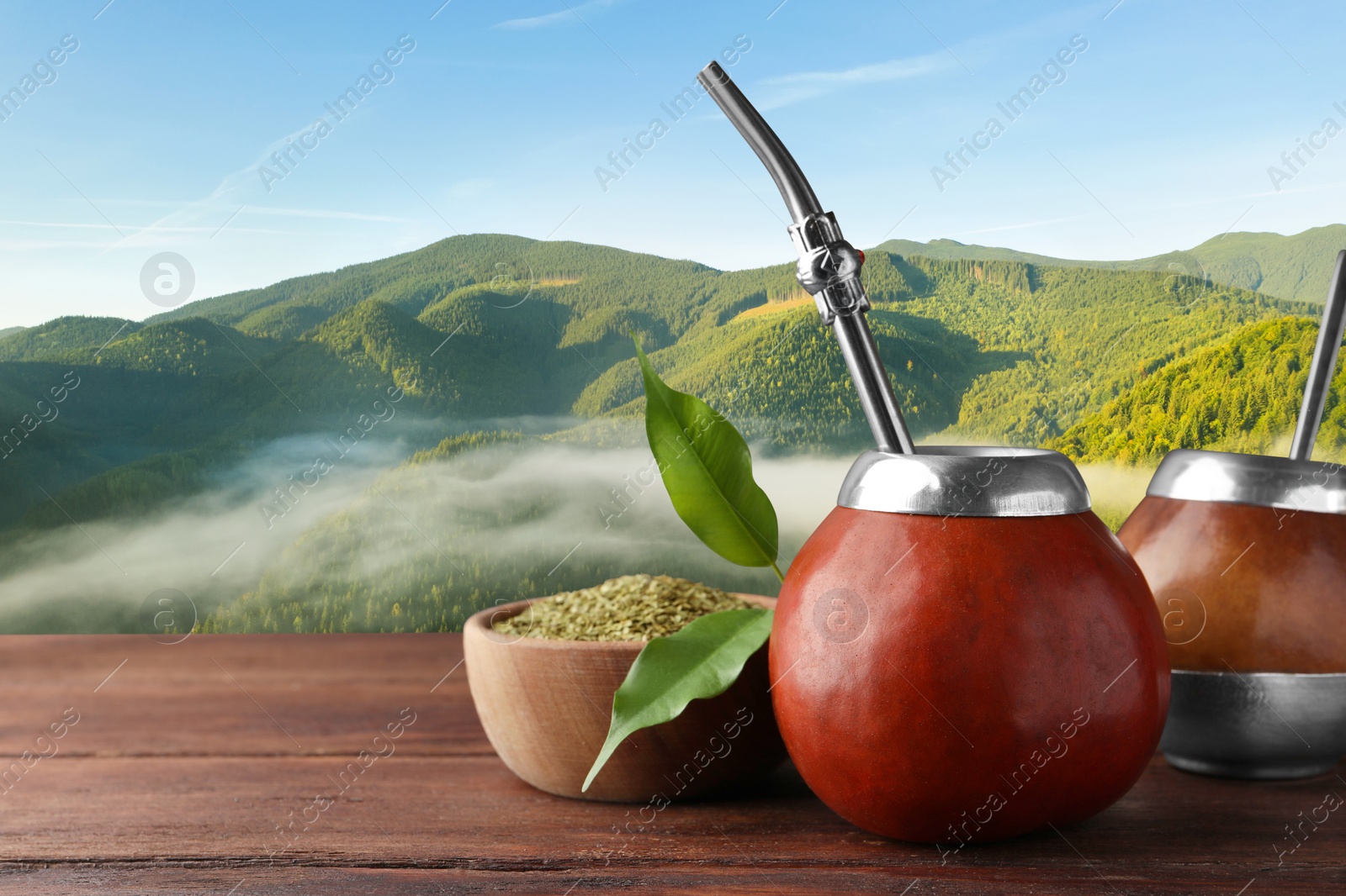 Image of Calabash with mate tea and bombilla on wooden table and beautiful view of mountain landscape, space for text