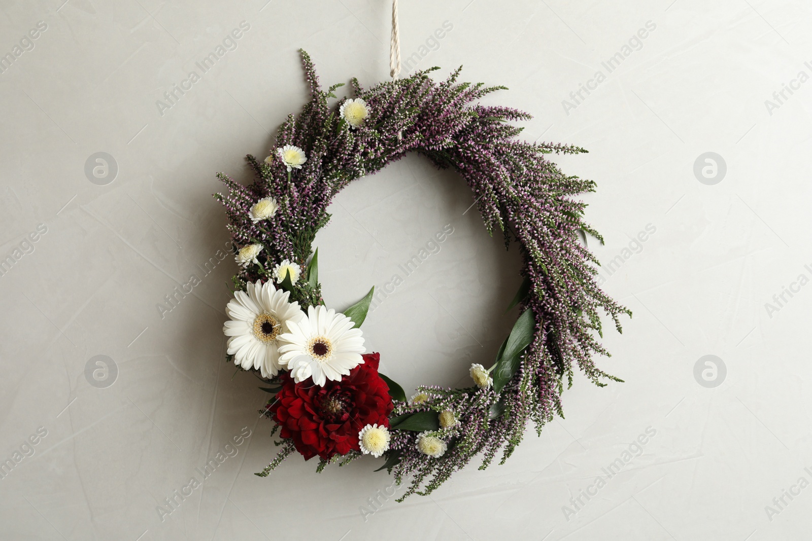 Photo of Beautiful autumnal wreath with heather flowers hanging on light grey background. Space for text