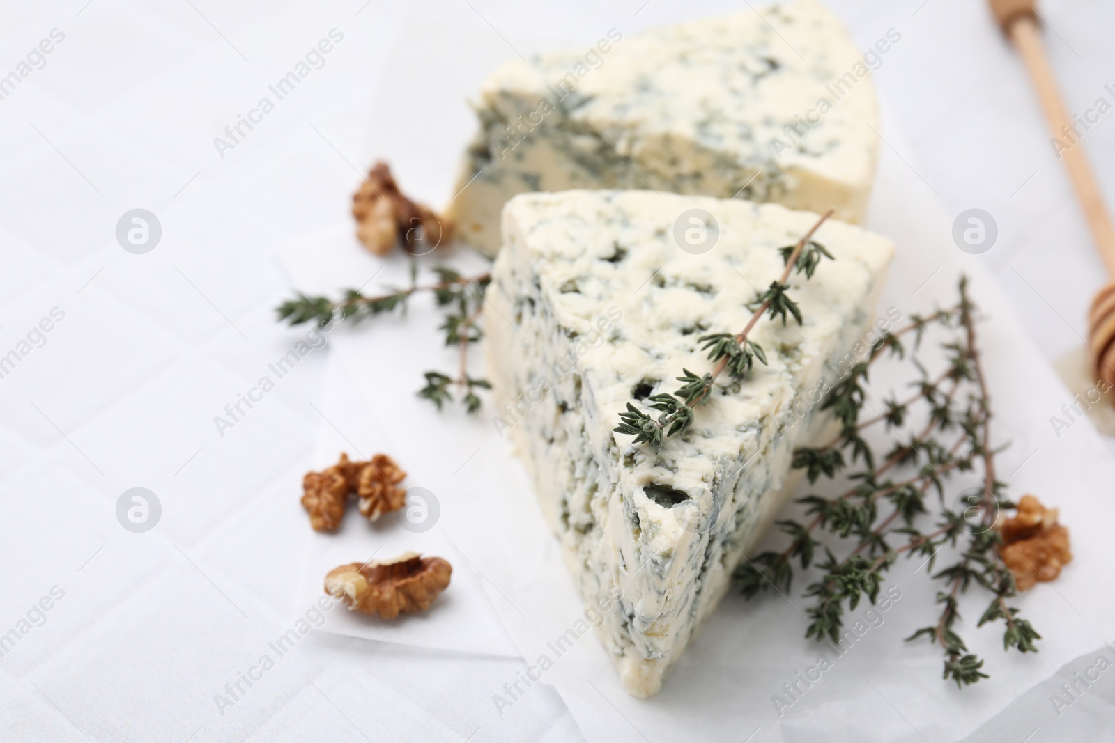 Photo of Tasty blue cheese with thyme, walnuts and honey dipper on white table, closeup. Space for text