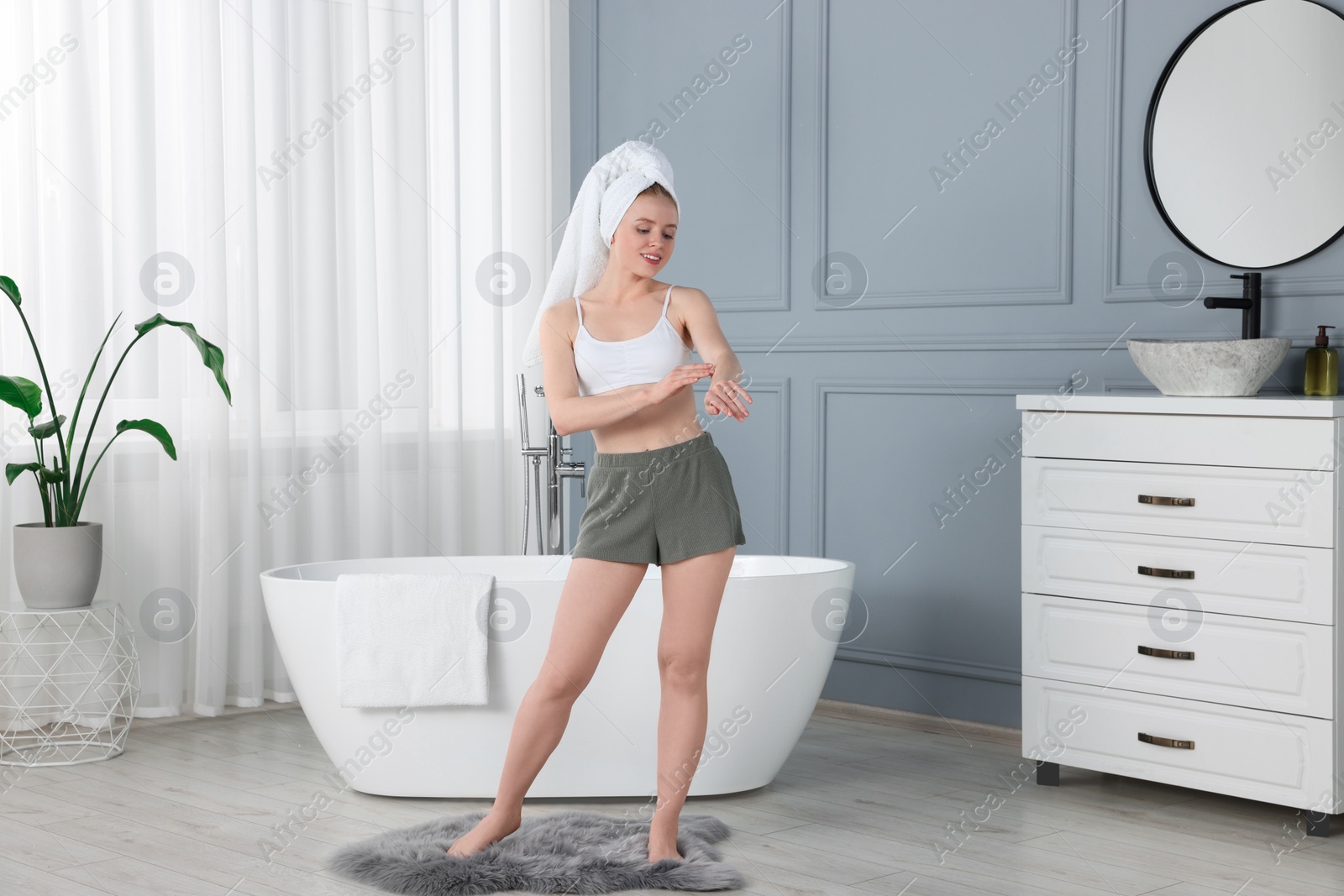 Photo of Beautiful young woman applying body cream onto arm in bathroom