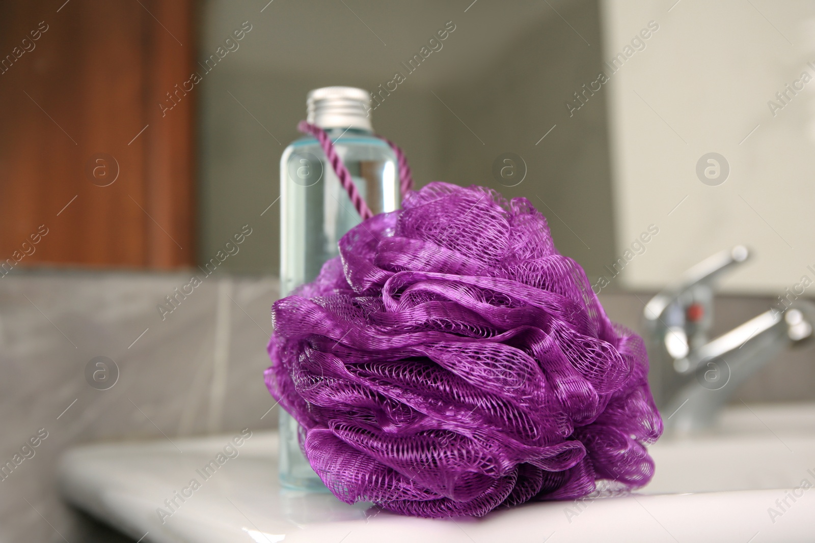 Photo of Purple shower puff and bottle of body wash gel on sink in bathroom