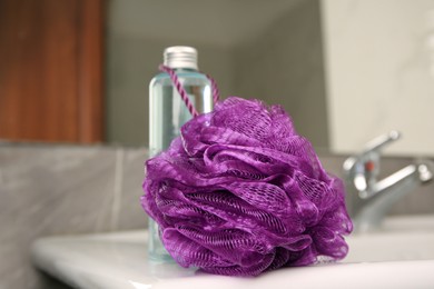 Photo of Purple shower puff and bottle of body wash gel on sink in bathroom