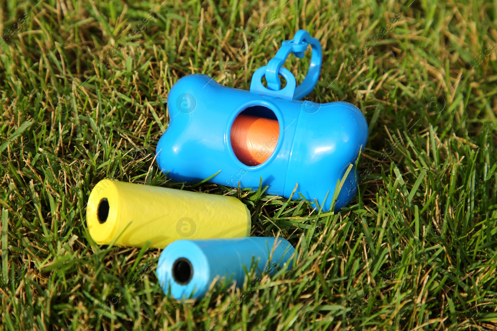 Photo of Rolls of colorful dog waste bags on green grass outdoors