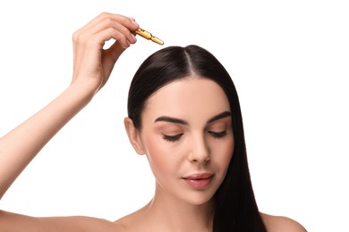 Beautiful young woman using ampoule for hair treatment on white background