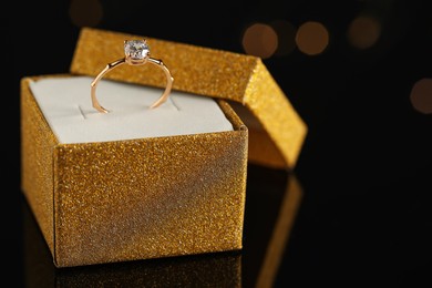 Beautiful engagement ring in box against blurred festive lights, space for text