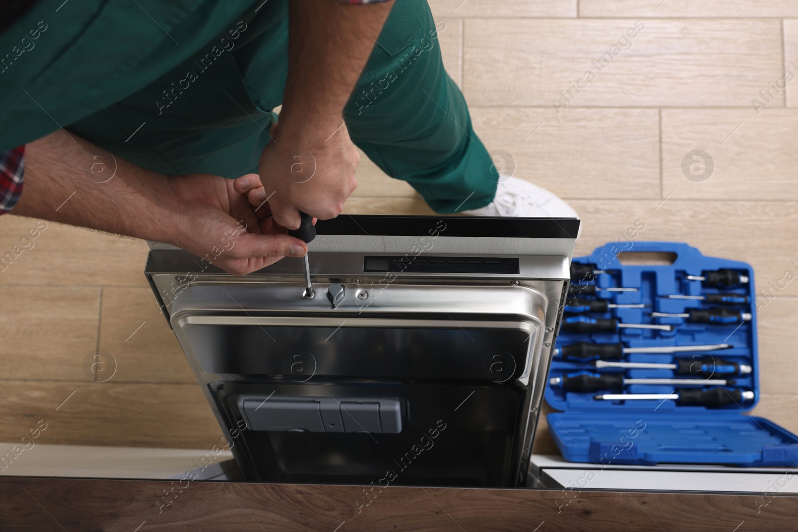 Photo of Serviceman repairing dishwasher's door with screwdriver indoors, closeup