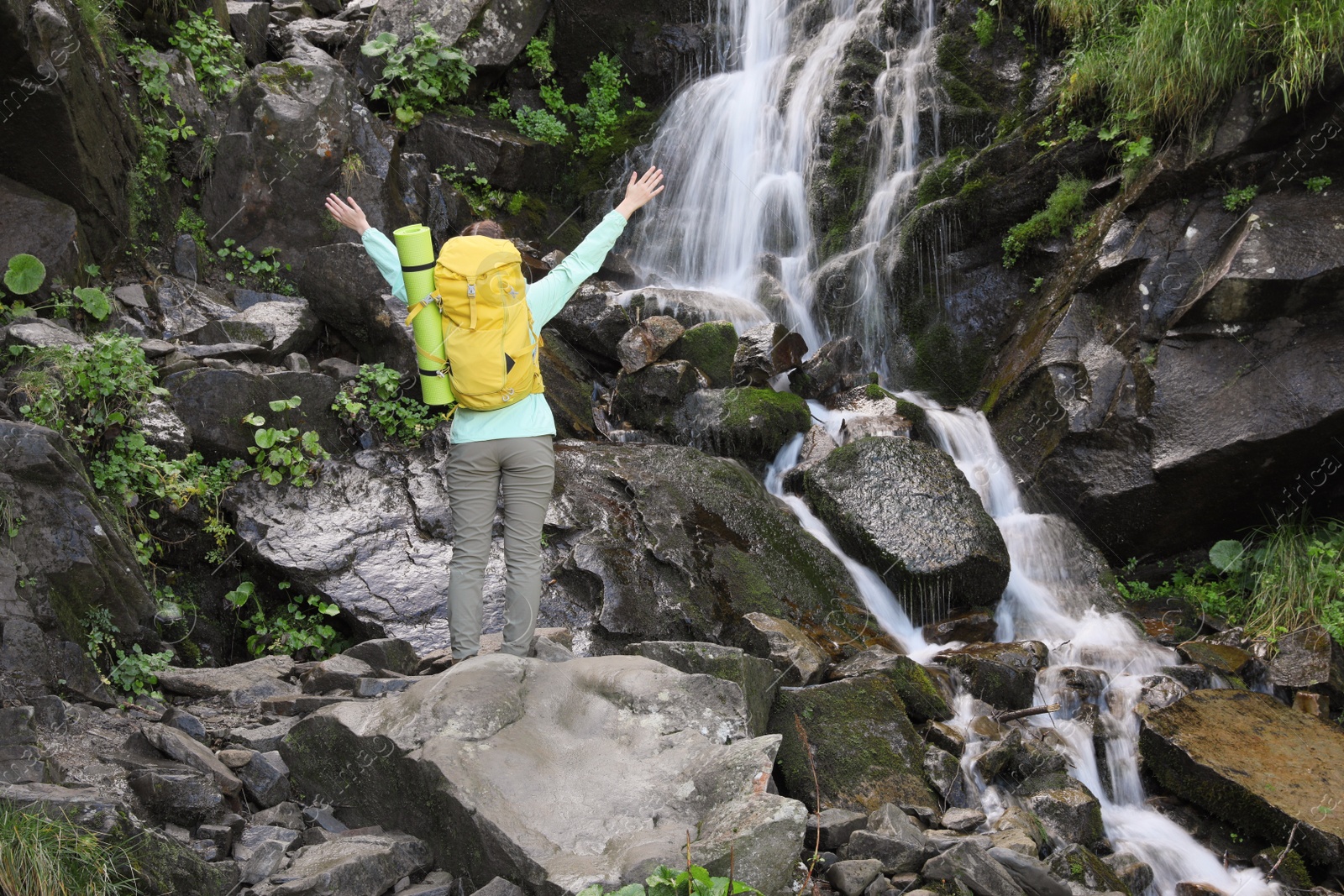 Photo of Happy tourist with backpack near mountain waterfall, back view