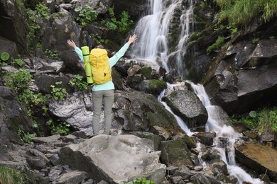 Photo of Happy tourist with backpack near mountain waterfall, back view