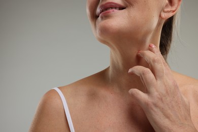 Mature woman touching her neck on grey background, closeup