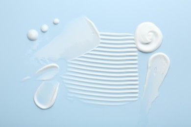 Photo of Samples of face cream on light blue background, top view