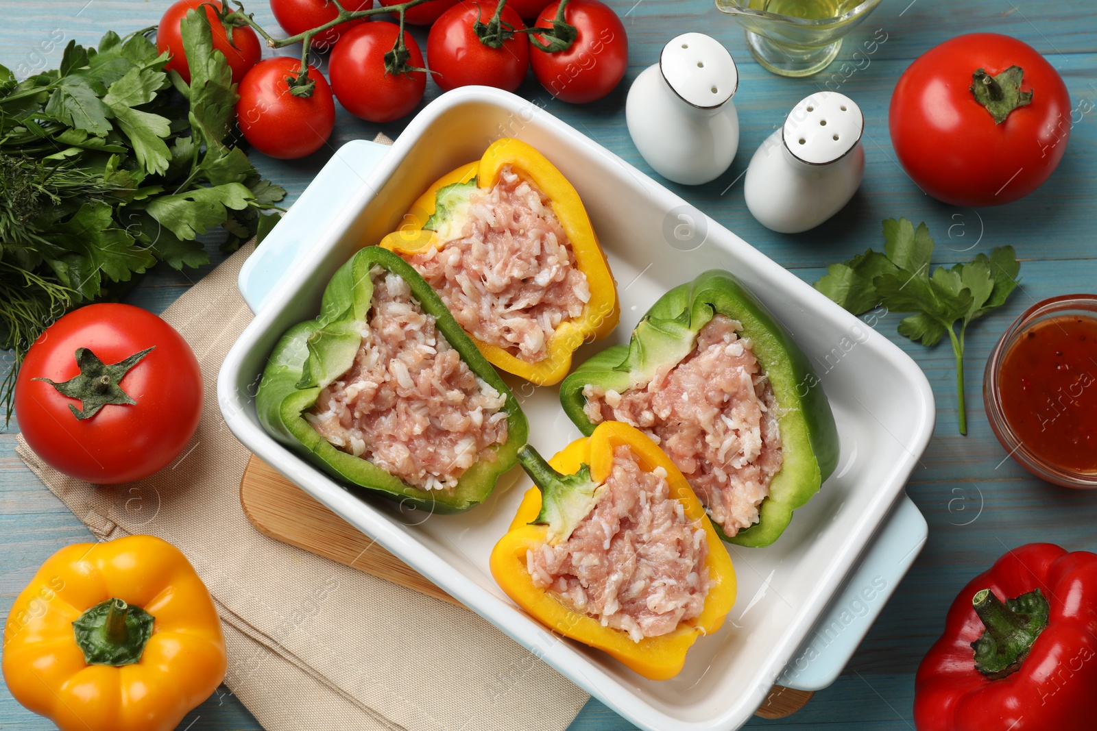 Photo of Raw stuffed peppers in dish and ingredients on wooden table, flat lay