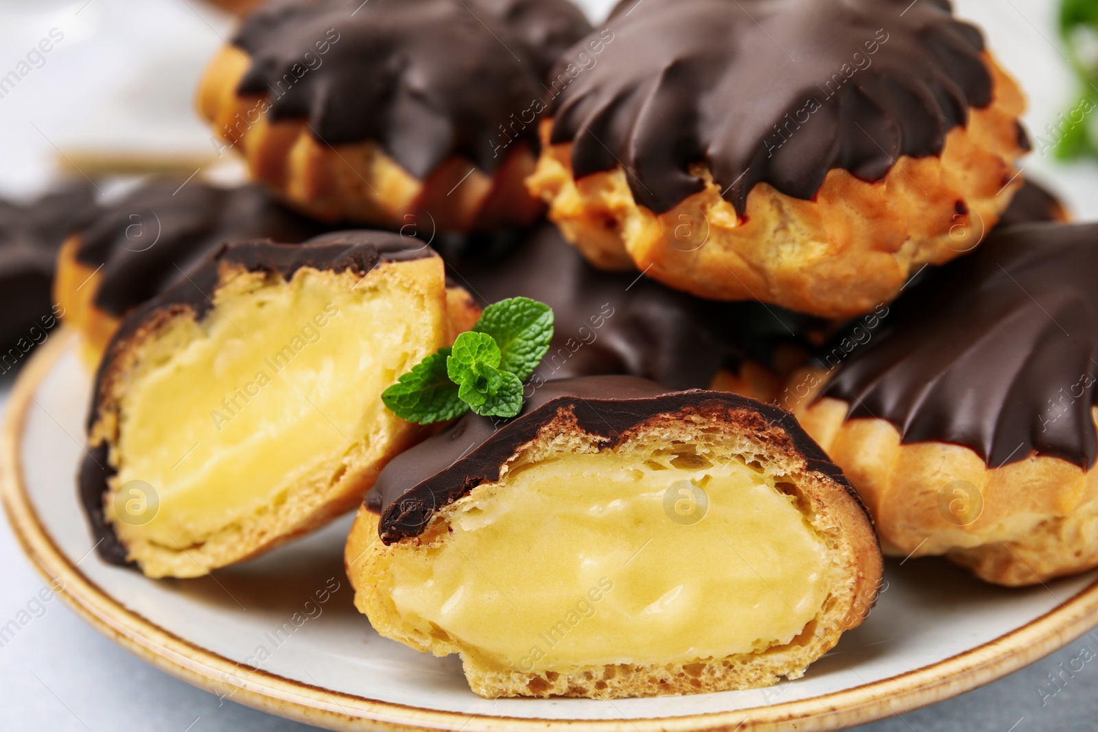 Photo of Delicious profiteroles with chocolate spread and cream on plate, closeup