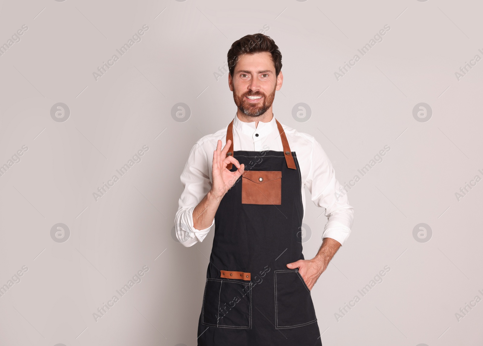 Photo of Smiling hairdresser showing ok gesture on light grey background