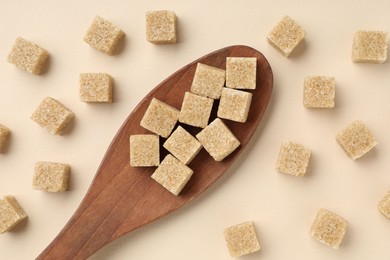 Photo of Brown sugar cubes and wooden spoon on beige background, flat lay