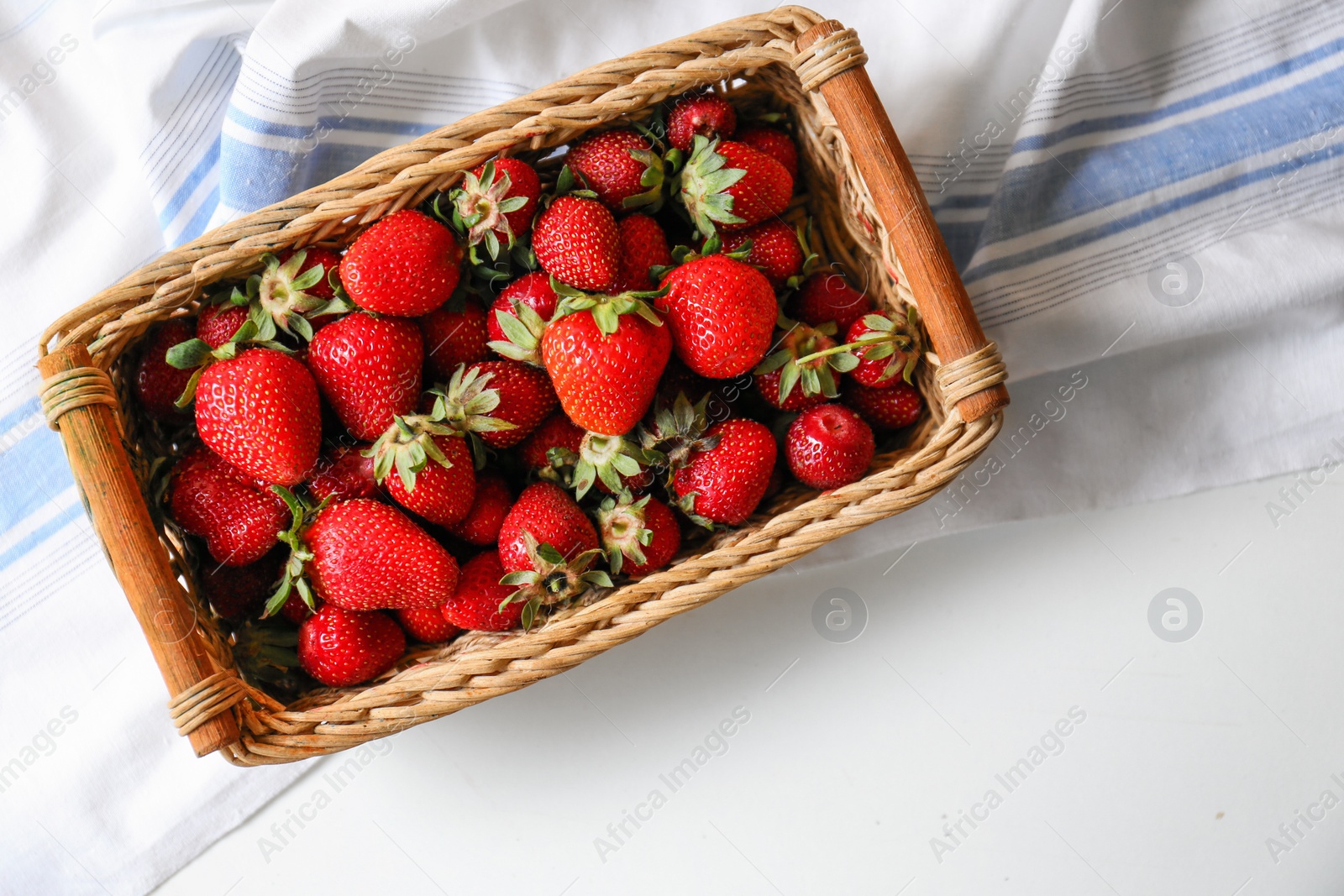 Photo of Wicker basket with ripe strawberries and napkin on white table, top view. Space for text