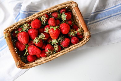 Wicker basket with ripe strawberries and napkin on white table, top view. Space for text