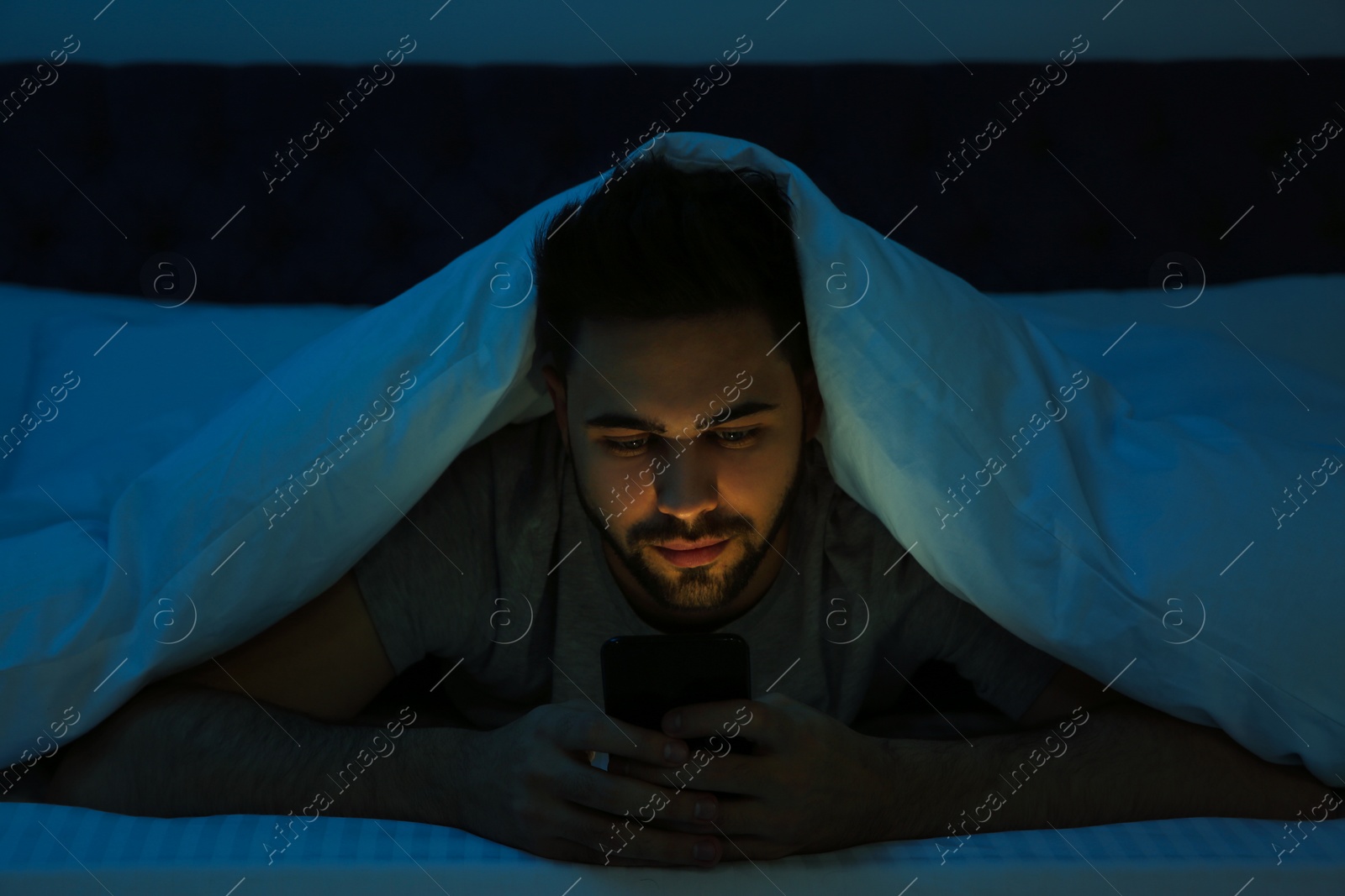 Photo of Young man addicted to smartphone in bed at night