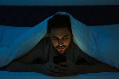 Young man addicted to smartphone in bed at night