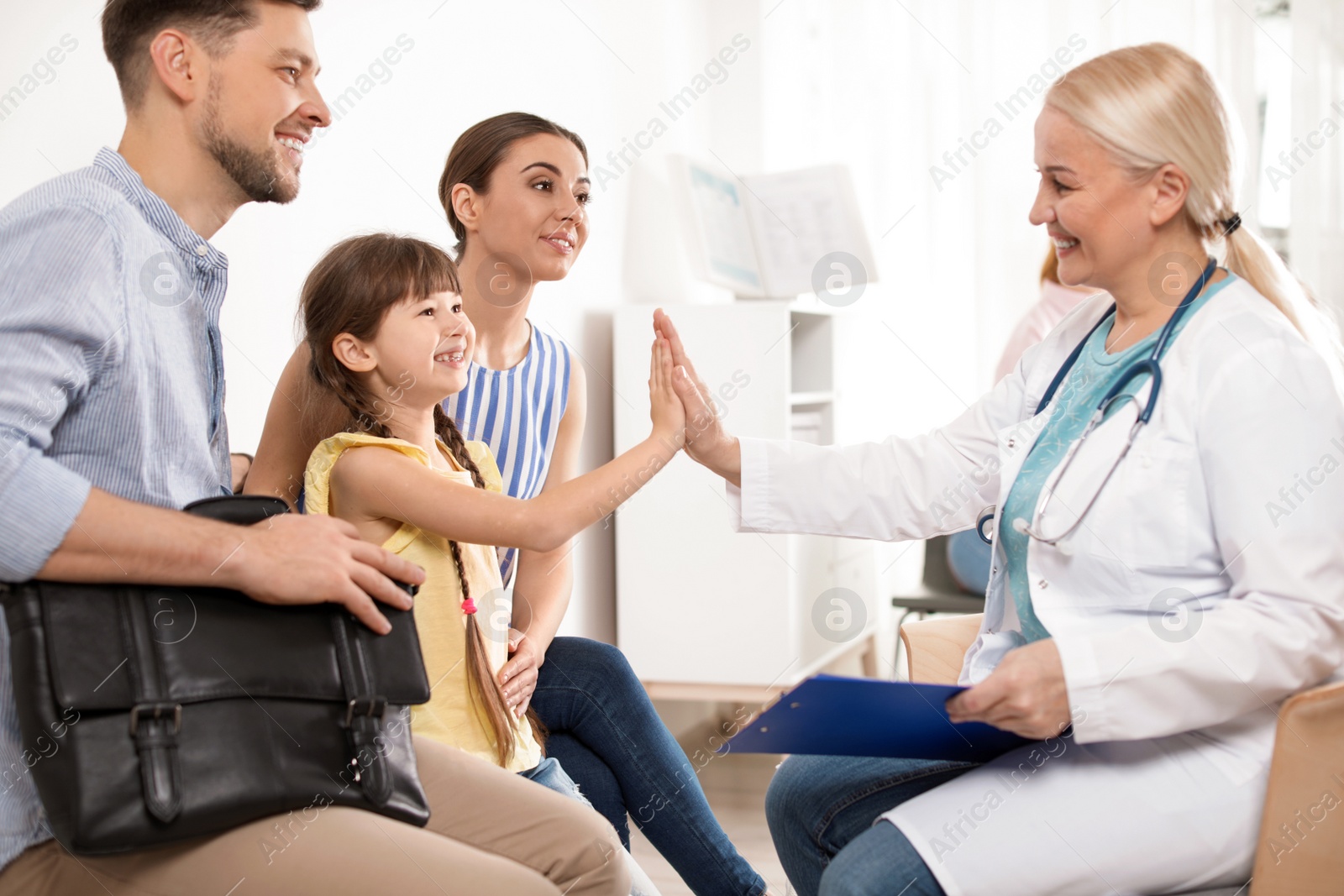 Photo of Cute child sitting with her parents and giving high five to doctor in hospital