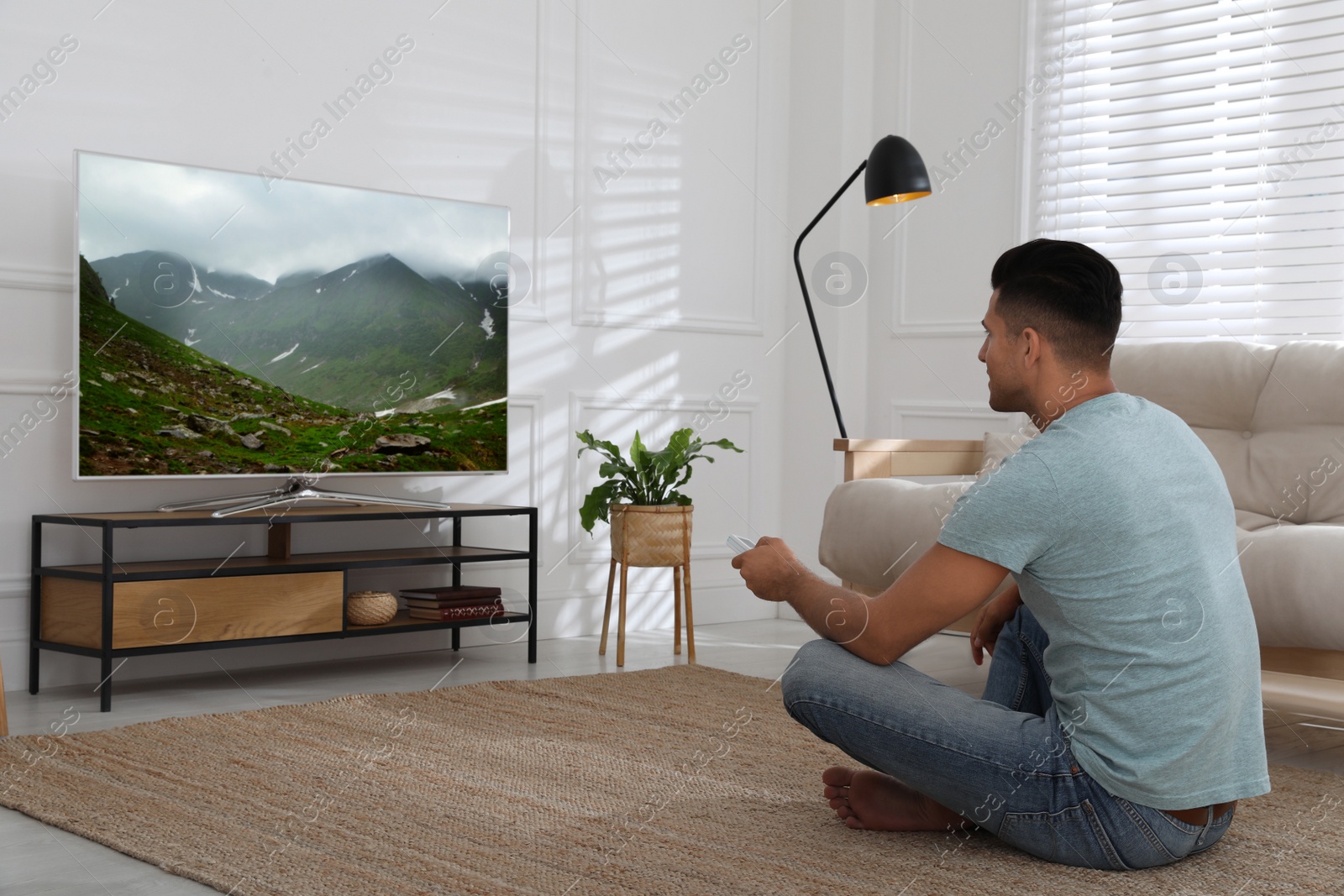 Photo of Man watching television at home. Living room interior with TV on stand