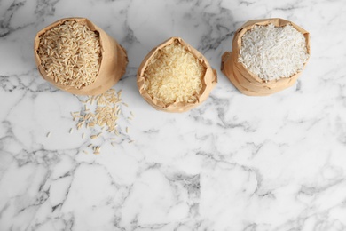 Photo of Paper bags with different types of rice on marble background, top view. Space for text