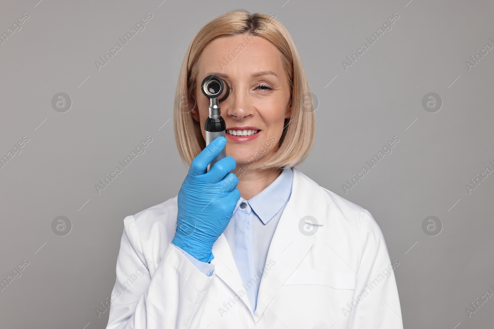 Photo of Happy dermatologist using dermatoscope on grey background