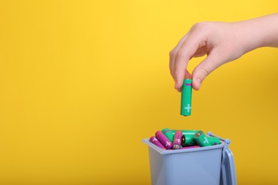 Photo of Woman putting used AA size battery into recycling bin on yellow background, closeup. Space for text