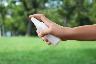 Woman with bottle of insect repellent spray outdoors, closeup